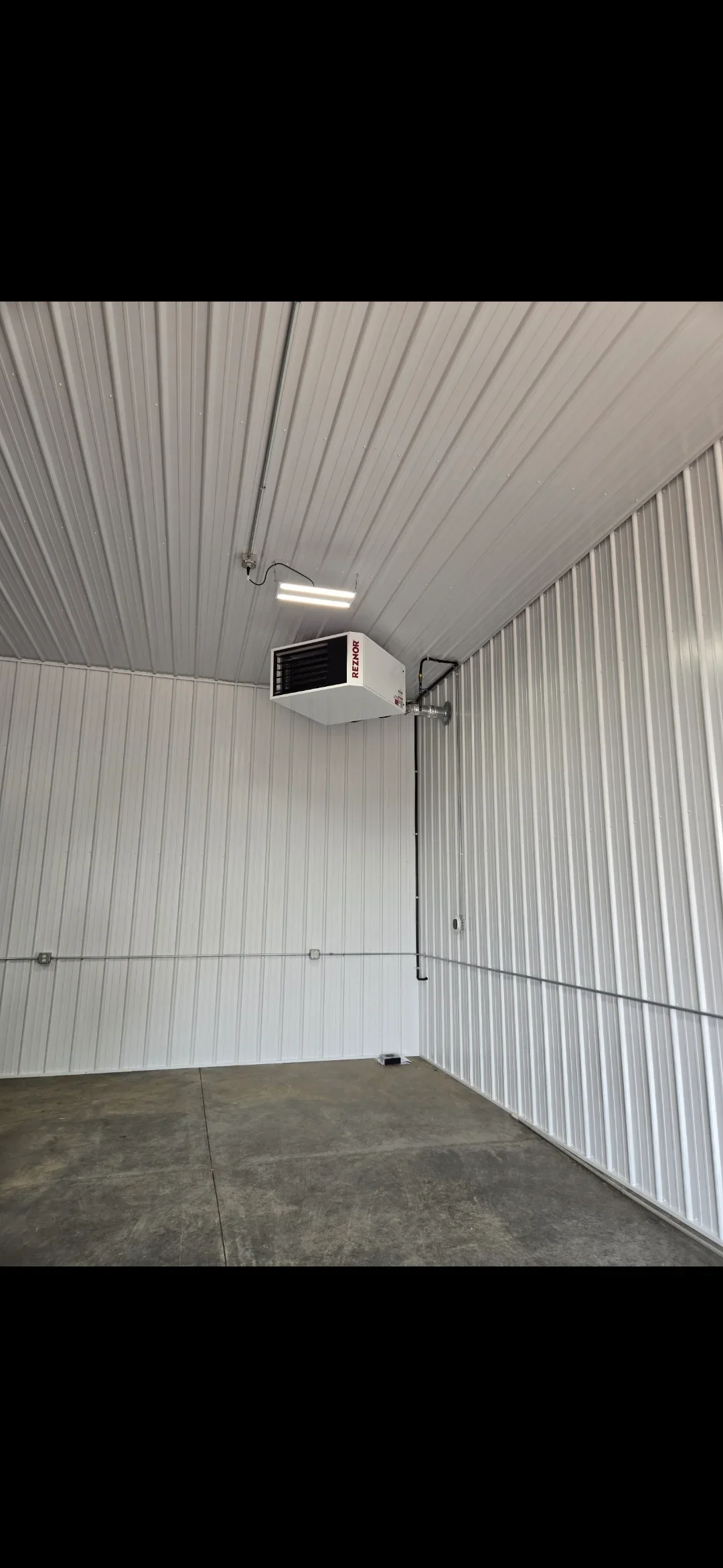 Ceiling-mounted commercial HVAC unit with ductwork in metal-frame building with corrugated walls