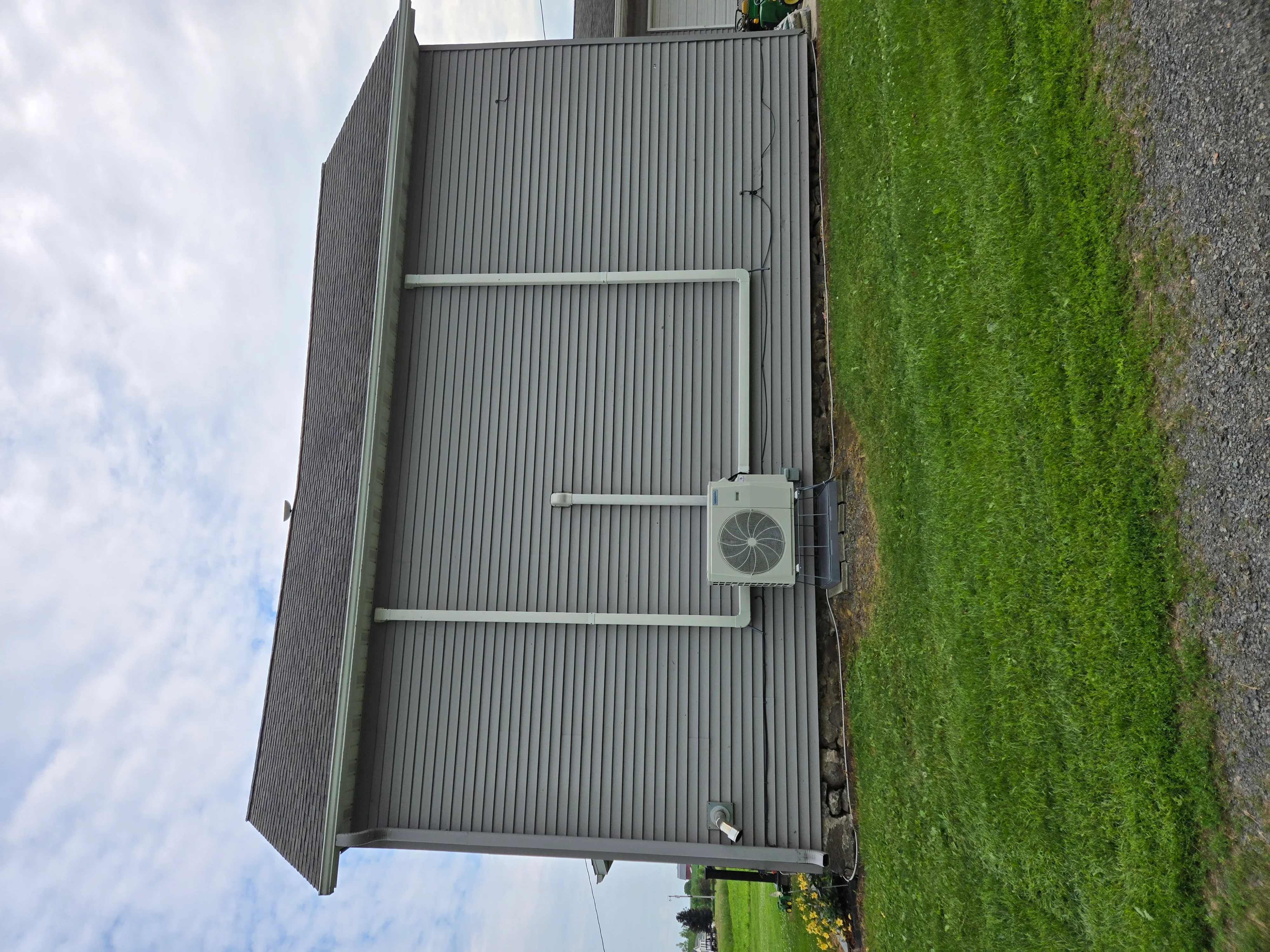 Heat pump unit mounted on corrugated metal building with refrigerant lines and conduit